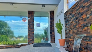 A hotel reception area with a stone wall, a reception desk, and a potted plant. - Hotel Conchas (Penha)