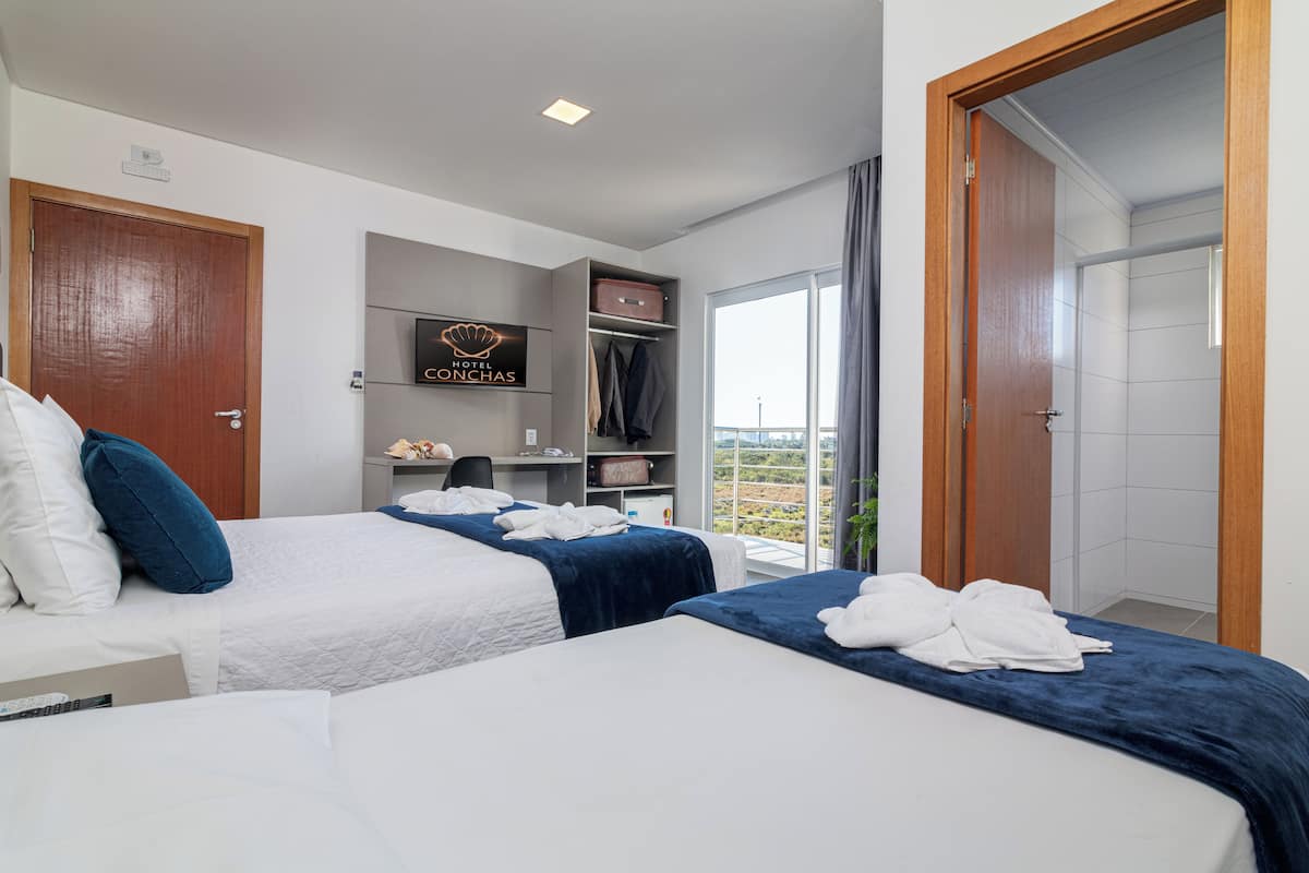 A hotel room with two beds, a desk, a wardrobe, and a balcony with a view.