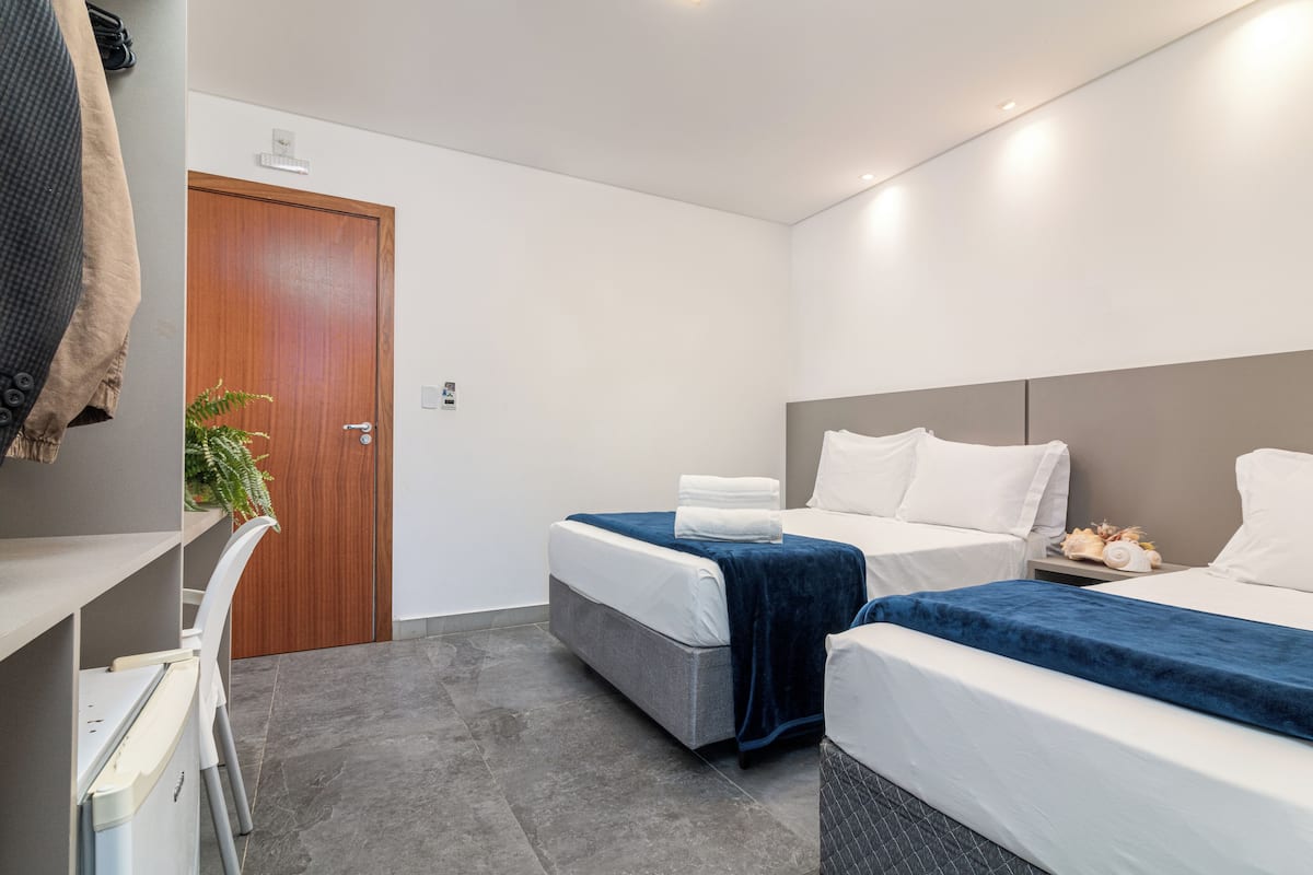 A modern hotel room with two beds, a desk, and a door.