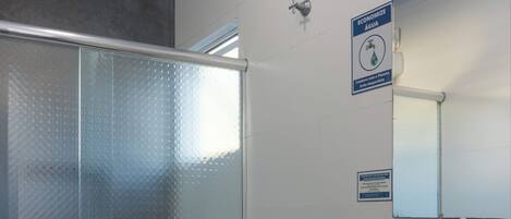 Egy modern fürőszoba, amely tartalmaz egy WC-t, egy üvegfalas zuhanykabint, egy mosdókagylót tükörrel, és egy törölközőtartót.