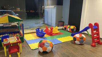 Uma área de recreação com tapetes coloridos, uma mesinha com brinquedos e um carrinho.