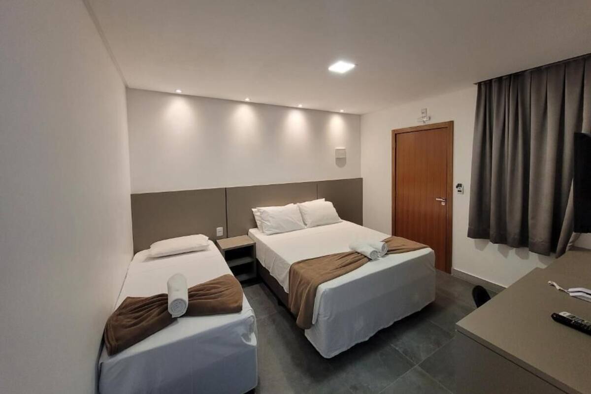 A hotel room with two beds, a desk, a TV, and a door.