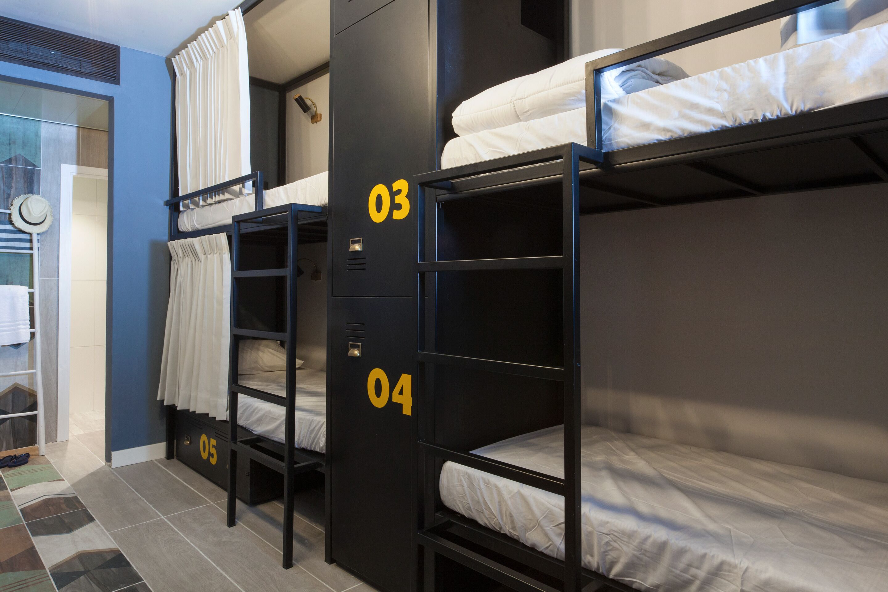 A dormitory room with bunk beds labeled 03, 04, and 05, a mirror, and a towel rack.