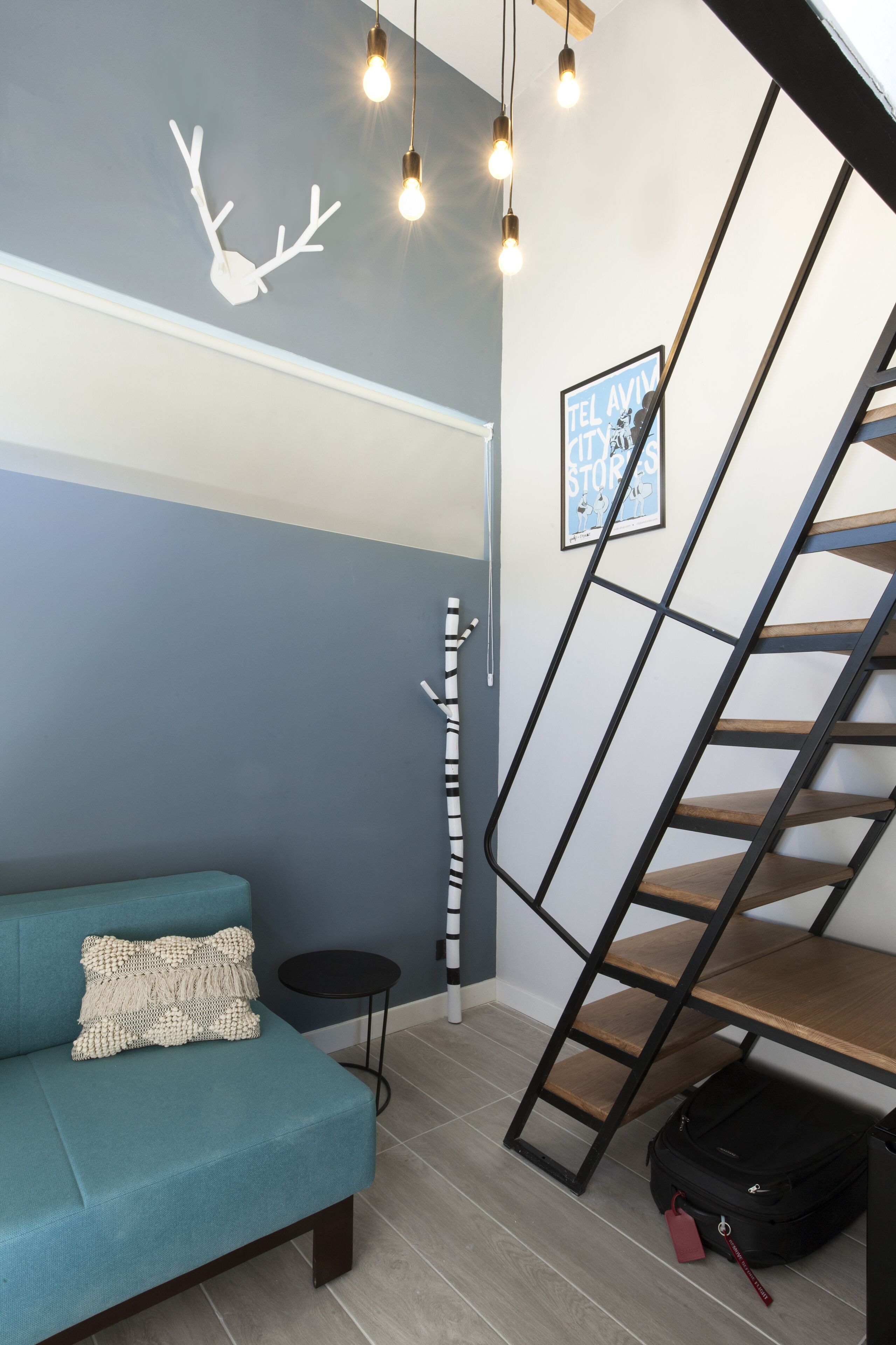 Een moderne kamer met een blauwgroene bank, een zwarte laddertrap, een wandlamp en een ingelijst kunstwerk.