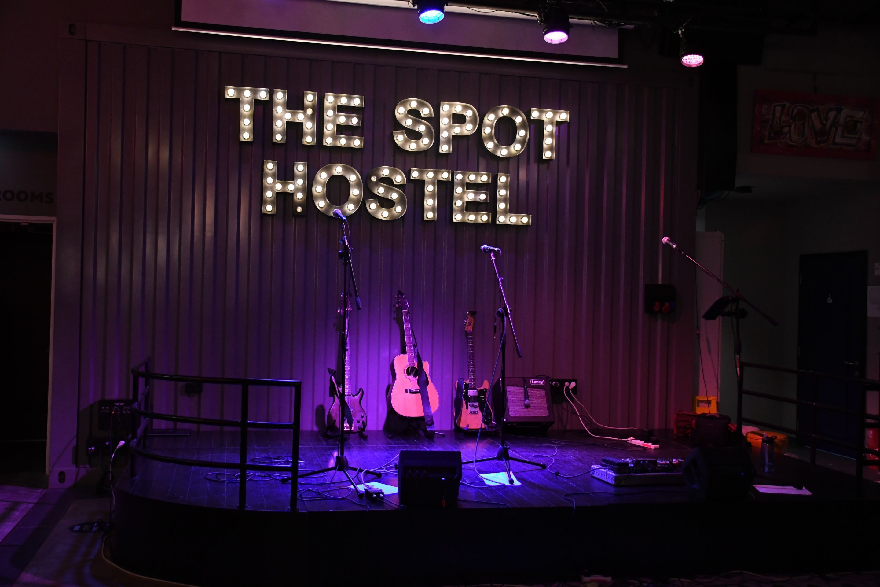 A stage with musical instruments and microphones, labeled "THE SPOT HOSTEL".