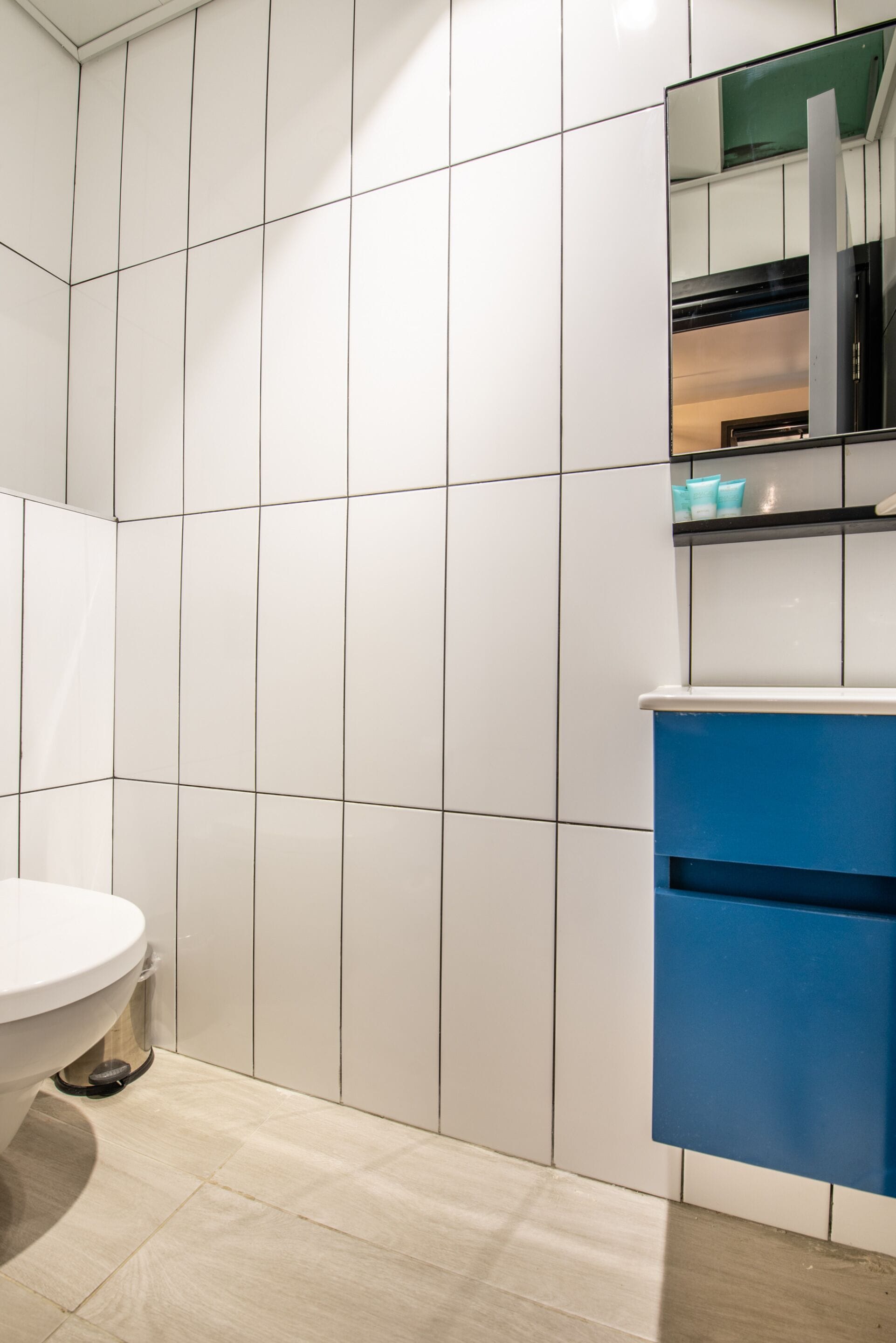 Een badkamer met witte betegelde wanden, een wit toilet en een blauwe wastafel met spiegel.
