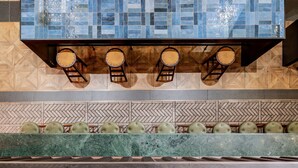 A bar area with a tiled backsplash, wooden stools, and a marble counter. - The Spot Hostel (Tel Aviv)