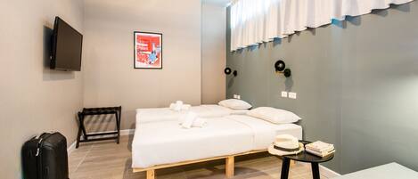 A hotel room with a bed, a TV, a suitcase, and a small table with a hat and books.