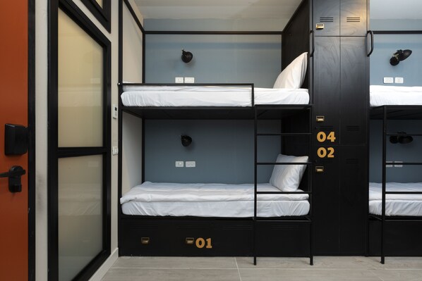 A bunk bed room with three levels, each with a mattress and pillows. There are wall-mounted lights above each bed.