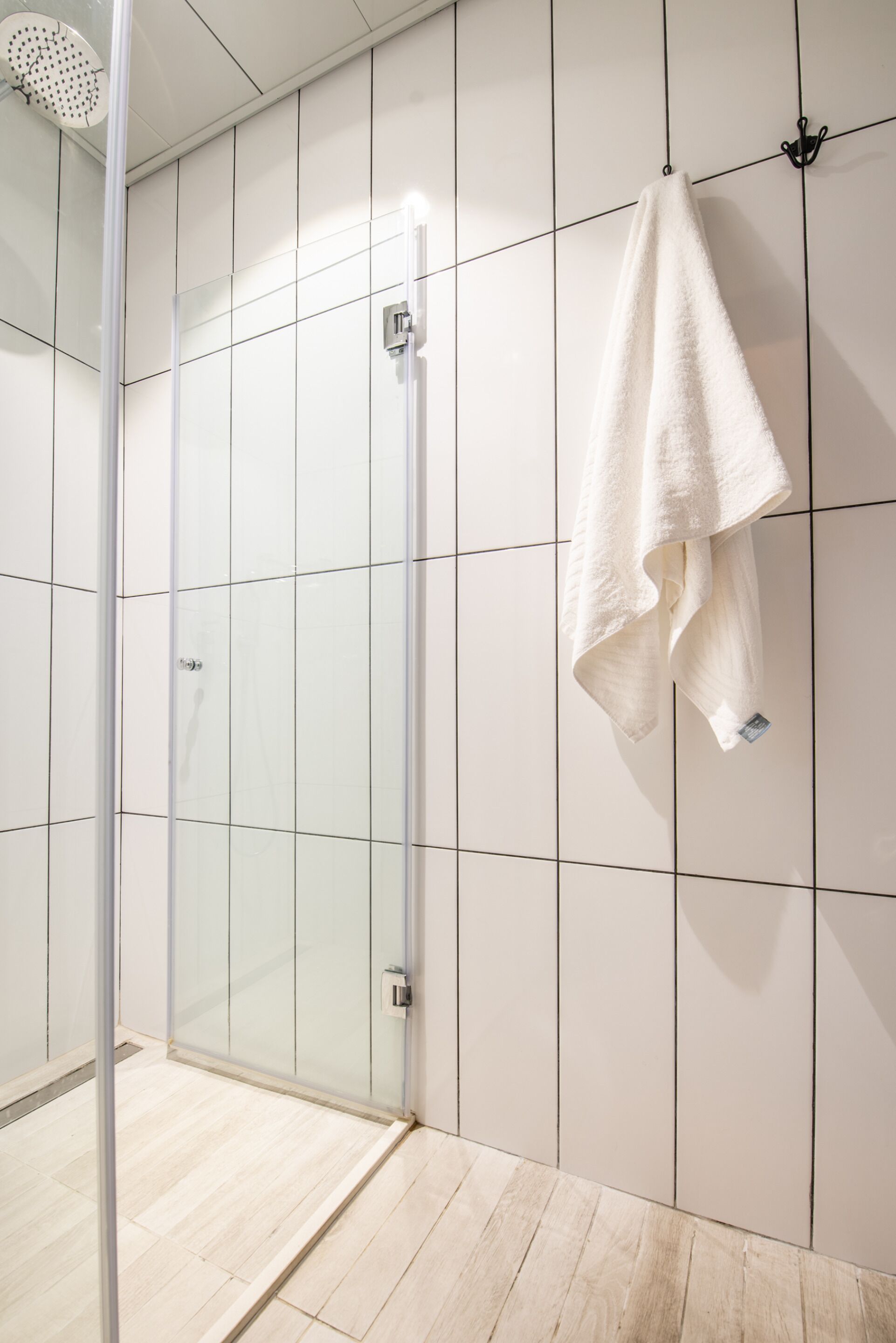 A modern bathroom with a glass shower enclosure, a white towel hanging on the wall, and a tiled floor.