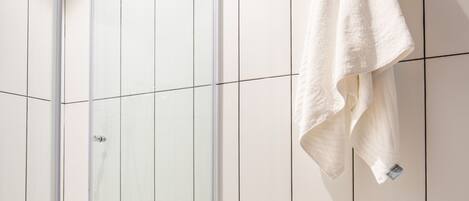 A modern bathroom with a glass shower enclosure, a white towel hanging on the wall, and a tiled floor.