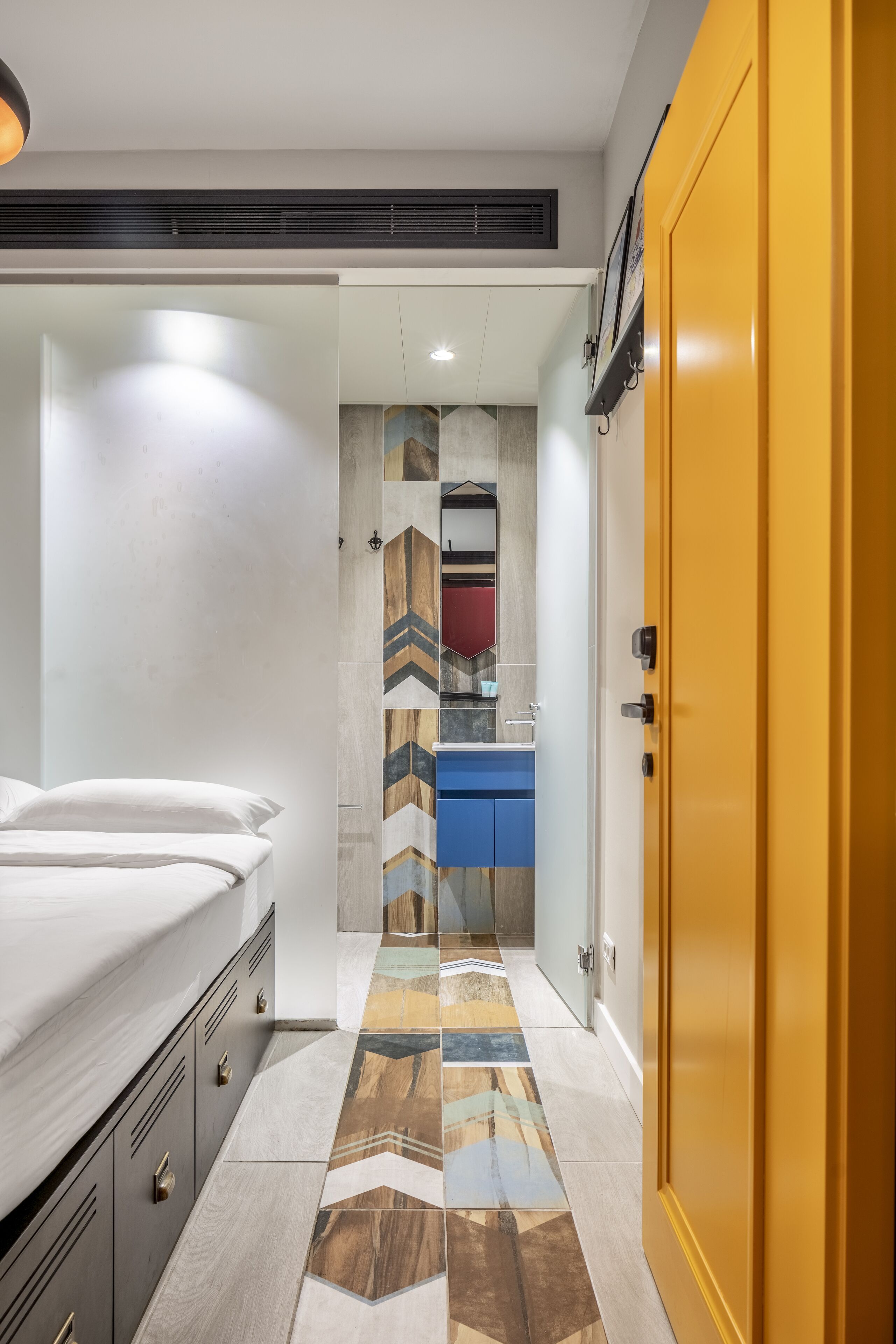 A hotel room with a bed, a wardrobe, a bathroom with a mirror, and a tiled floor.