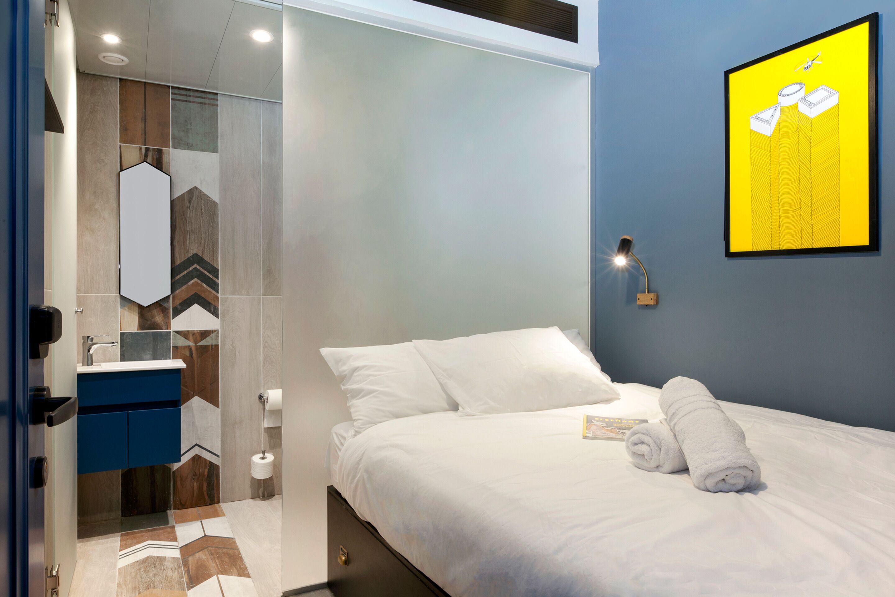 Una habitación de hotel moderna con una cama, un baño con espejo y una obra de arte colgada en la pared.