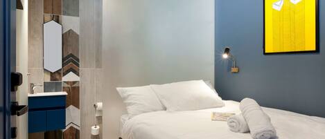 Una habitación de hotel moderna con una cama, un baño con espejo y una obra de arte colgada en la pared.