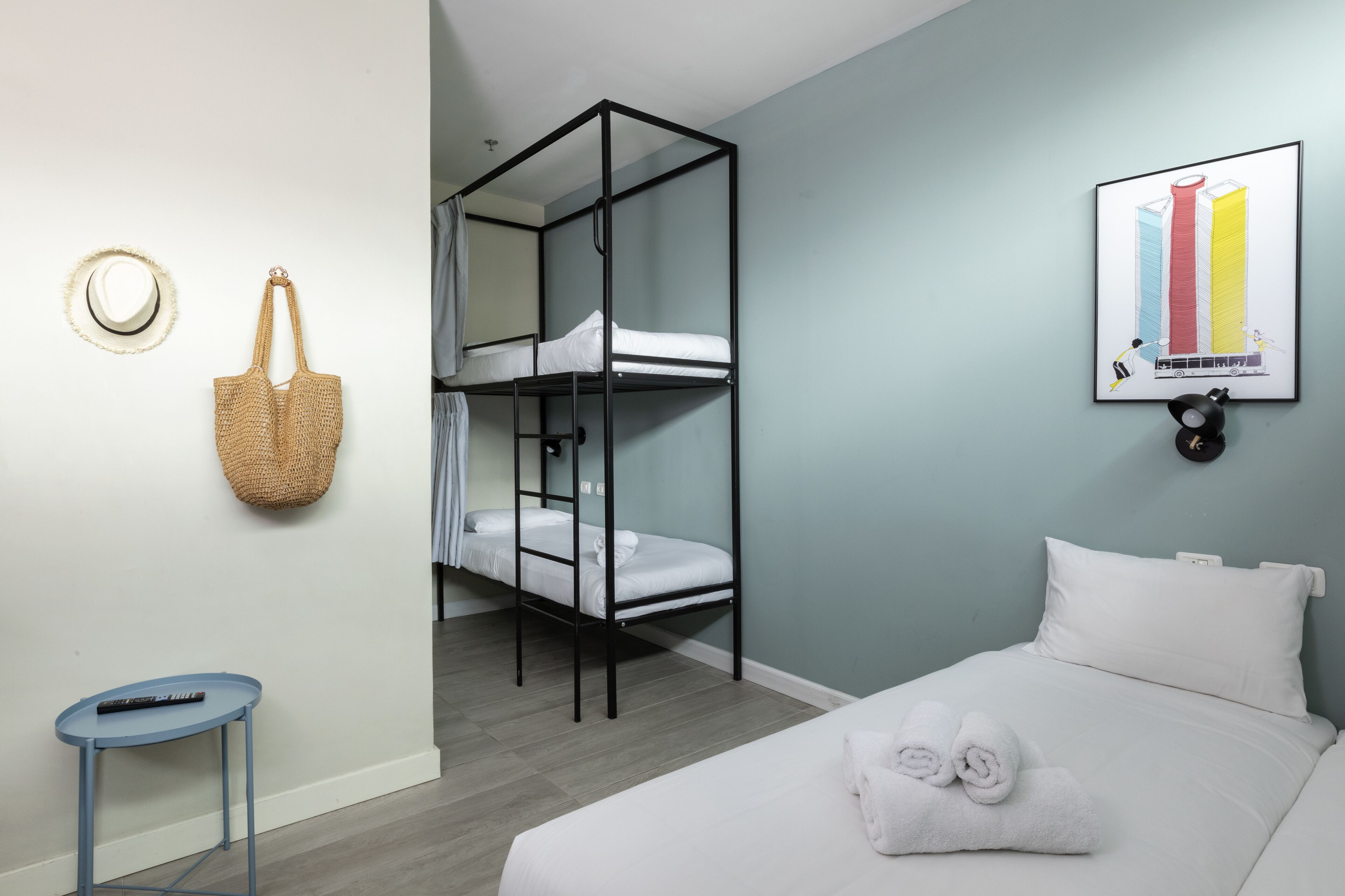 A room with bunk beds, a single bed, a small table, a wall-mounted basket, and a framed picture.