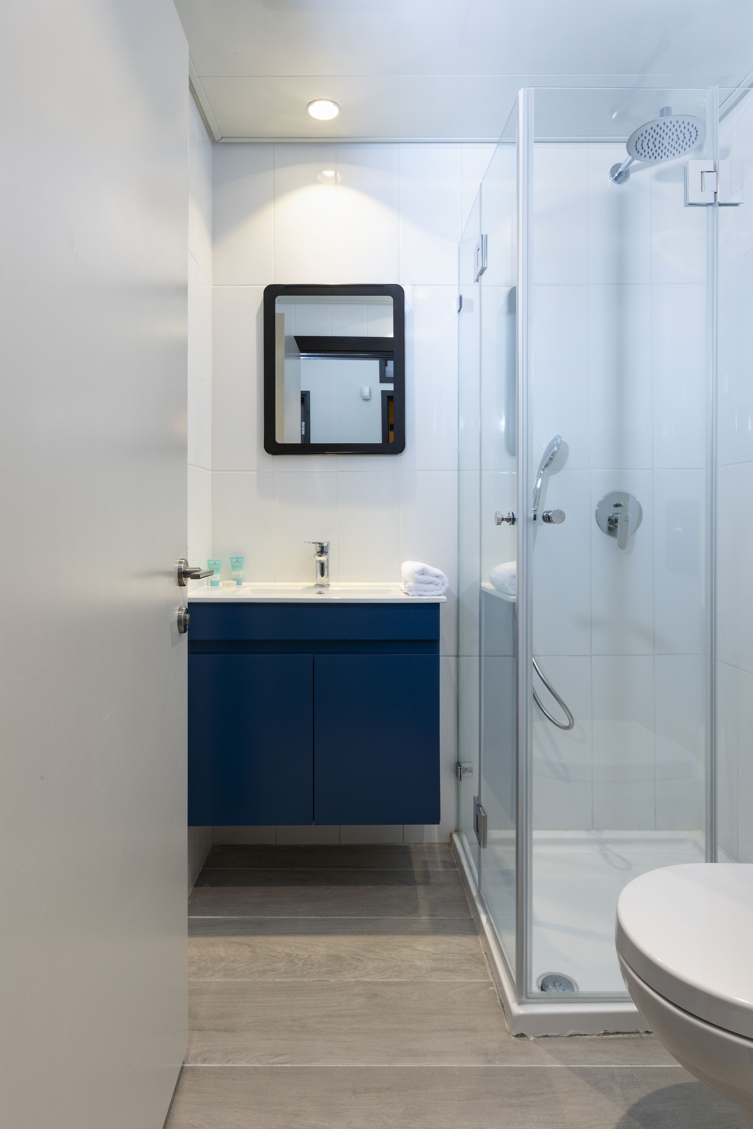 Un baño moderno con una cabina de ducha de vidrio, un lavamanos blanco con un espejo encima y un mueble azul.