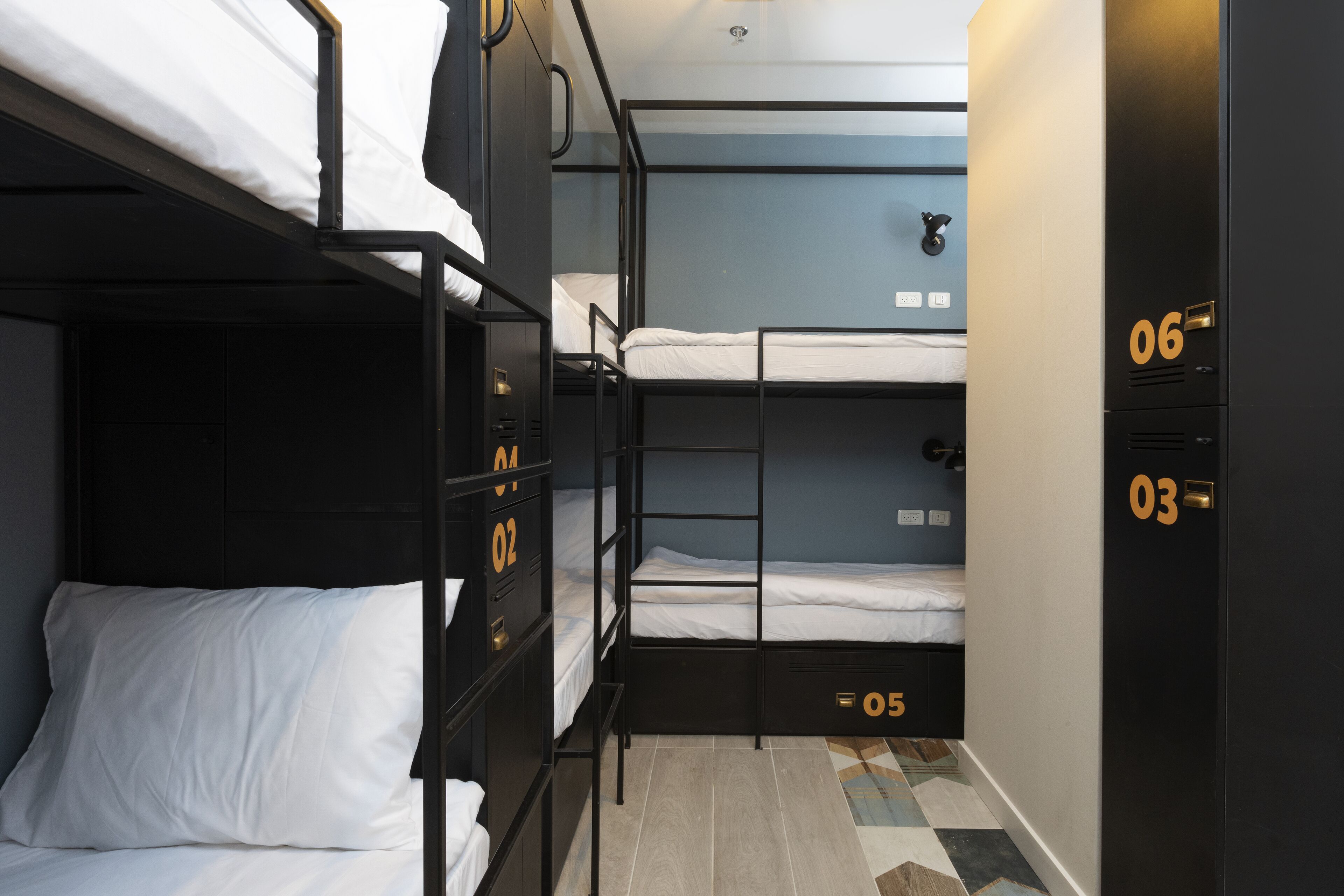 A compact room with bunk beds, a wardrobe with numbered compartments, and a patterned floor.