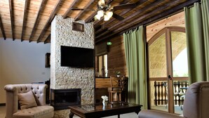A cozy living room with a stone fireplace, wooden ceiling beams, and a large window with curtains. - Palais Des Cedres (Barouk)