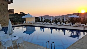 A poolside area with lounge chairs and umbrellas, a clear sky, and a sunset in the background. - Palais Des Cedres (Barouk)