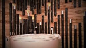 A spa room with a large, round, white bathtub, wooden slats on the walls, and a small table with a glass and a bottle. - Palais Des Cedres (Barouk)