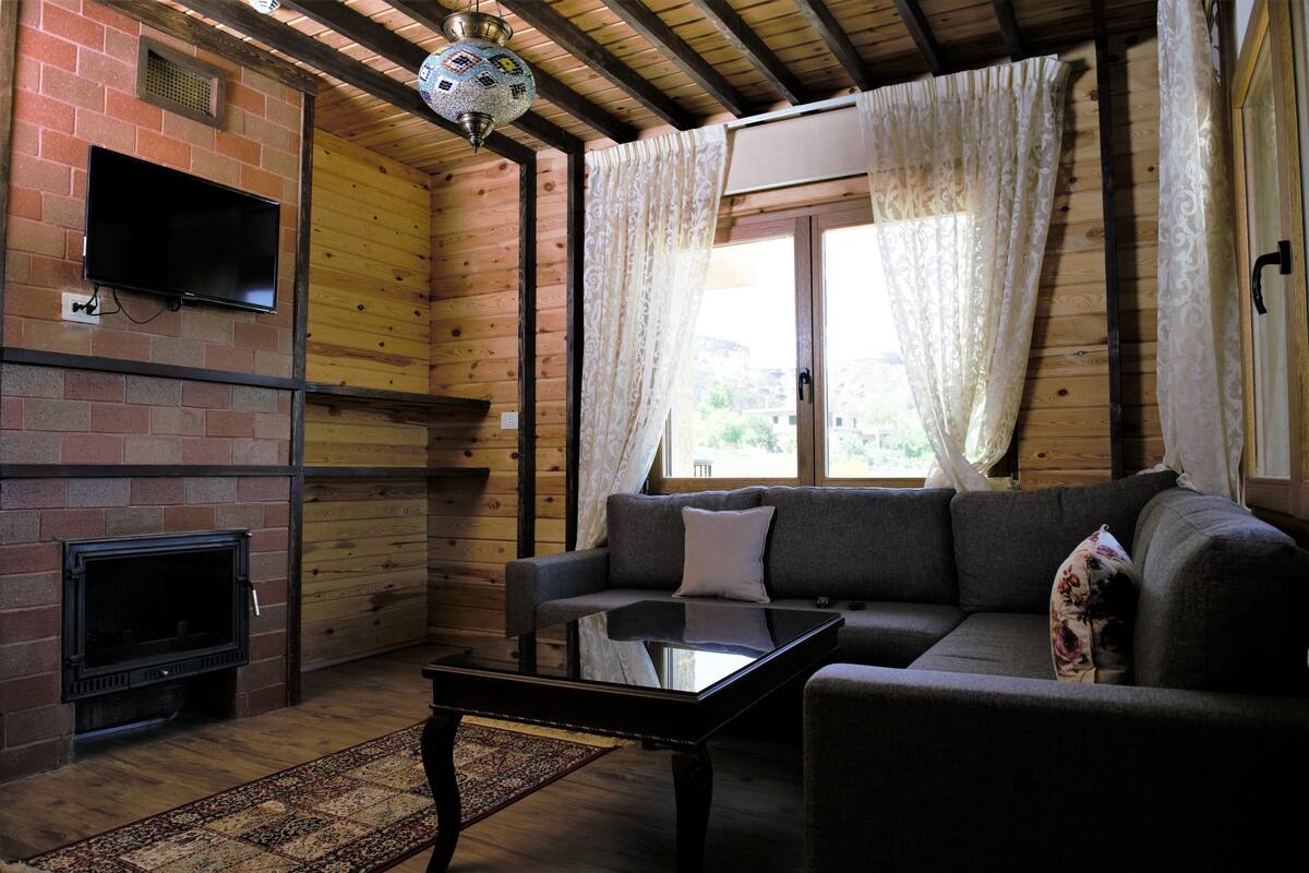 A cozy living room with a brick fireplace, a flat-screen TV mounted on the wall, a sofa with cushions, and a glass coffee table.