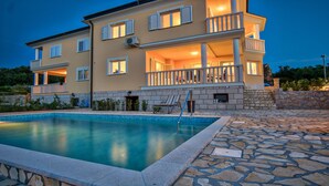Un bâtiment à deux étages doté d’une piscine, d’une terrasse en pierre et d’un balcon avec des balustrades.