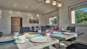 Un coin repas avec une longue table dressée pour le repas, un canapé et un tableau accroché au mur.
