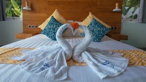 A hotel room with a wooden headboard, patterned pillows, and a bed with towels arranged in a swan shape. - Modern Oceanfront Luxury in the Unspoilt Beauty of the Original Bali (Seririt)