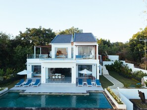 Une maison moderne à deux étages dotée d’une piscine, d’un espace salon extérieur et d’un balcon.