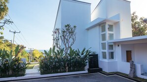 A modern building with a clean, white facade, large windows, and a well-maintained garden area with tropical plants. - Modern Oceanfront Luxury in the Unspoilt Beauty of the Original Bali (Seririt)