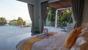 A modern hotel room with a large bed, a view of the ocean, and a balcony with a glass door. - Modern Oceanfront Luxury in the Unspoilt Beauty of the Original Bali (Seririt)