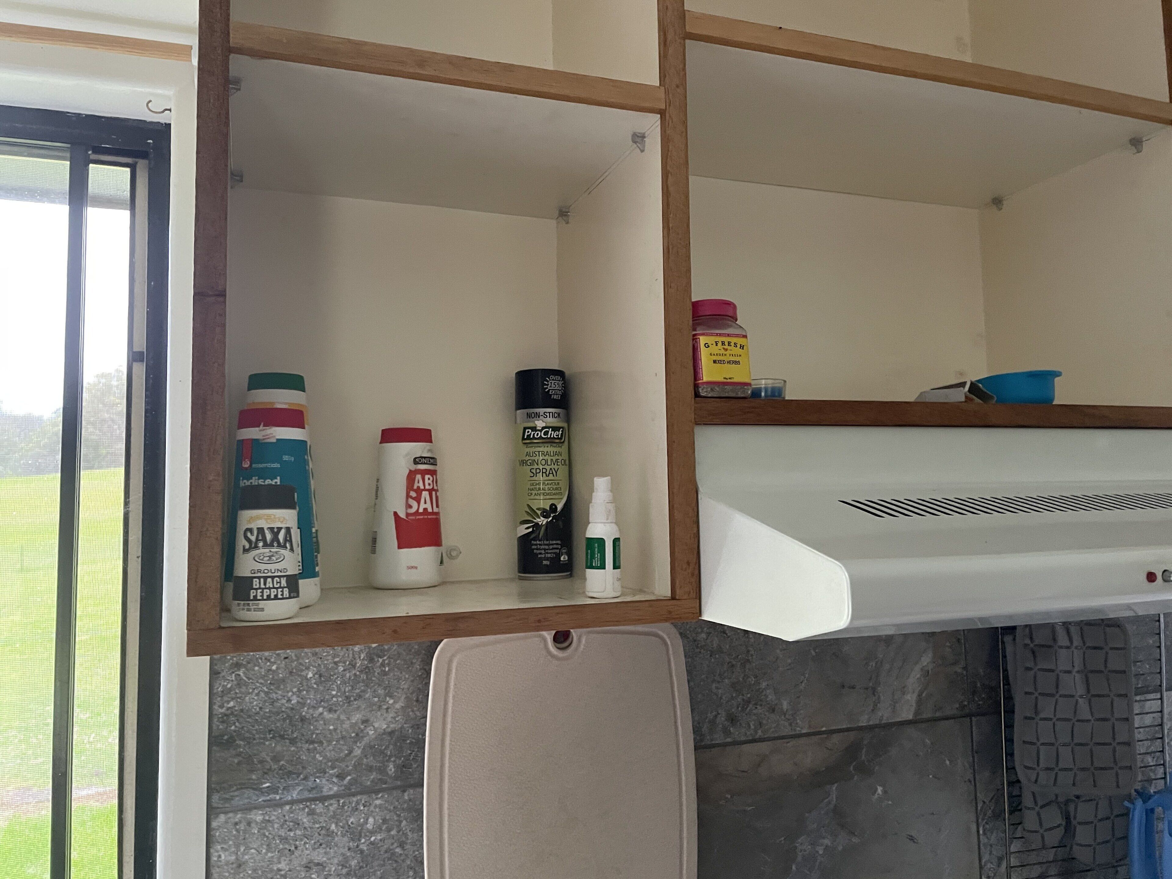 A kitchen with a built-in microwave and a shelf with various kitchen items.
