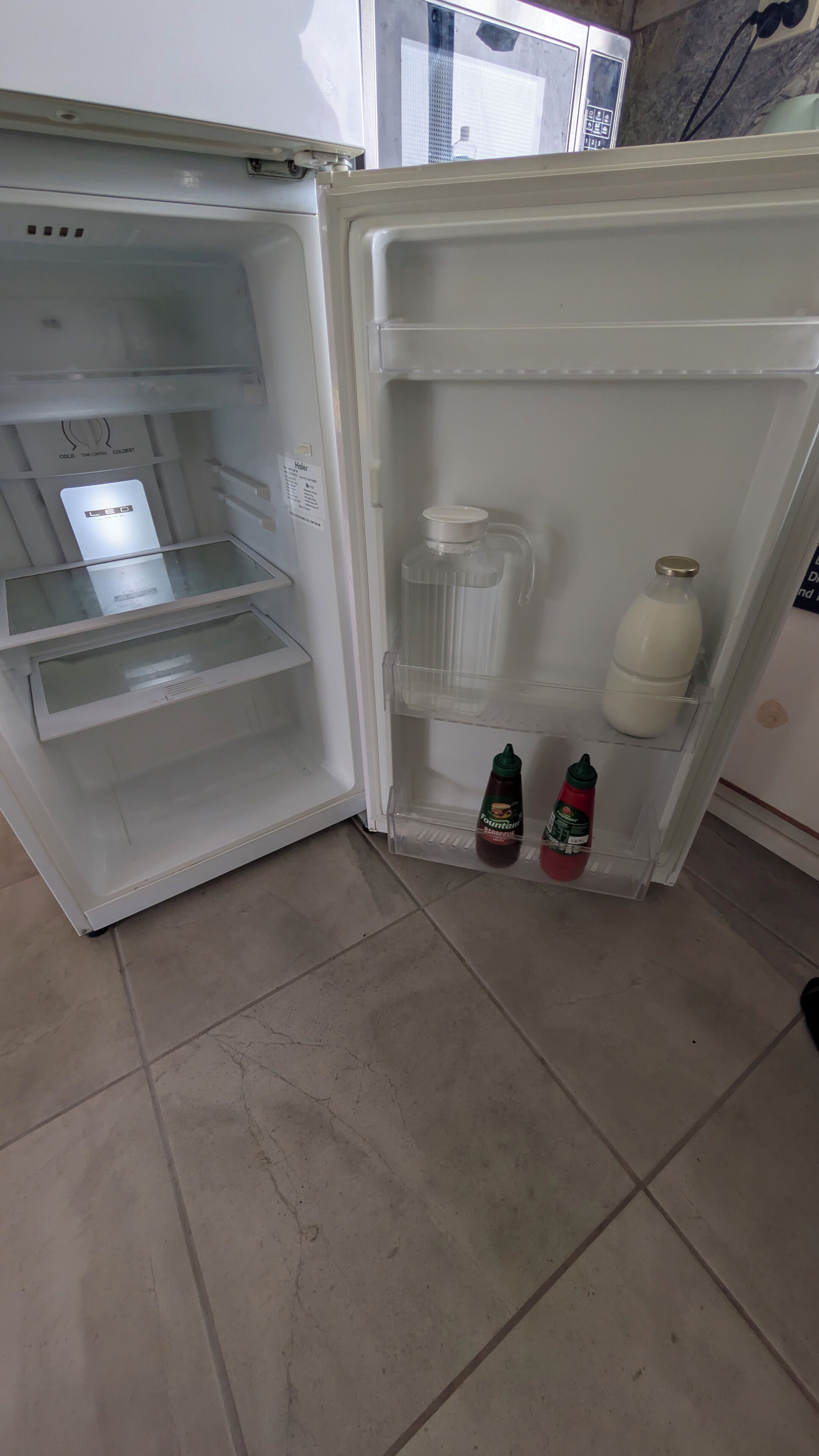 An open refrigerator with a freezer compartment on the left, a milk bottle, and two condiment bottles on the door shelf.