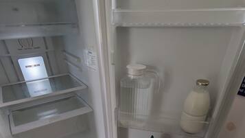 An open refrigerator with a freezer compartment on the left, a milk bottle, and two condiment bottles on the door shelf.