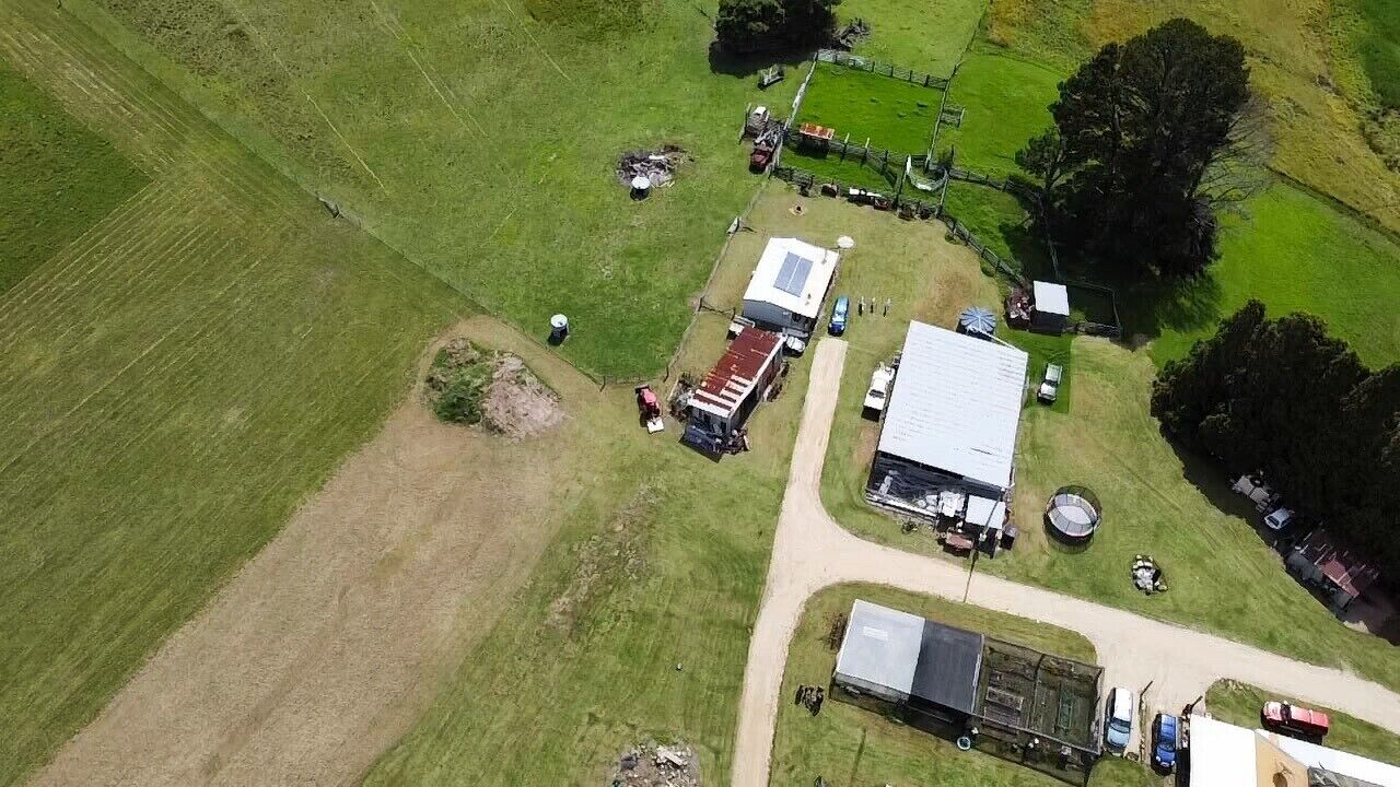 An aerial view of a rural property with a large barn, a smaller building, and a fenced area with vehicles.