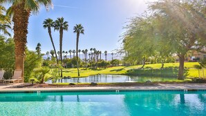 Ein Schwimmbecken mit klarem, blauem Wasser, umgeben von Palmen und einem Golfplatz im Hintergrund.