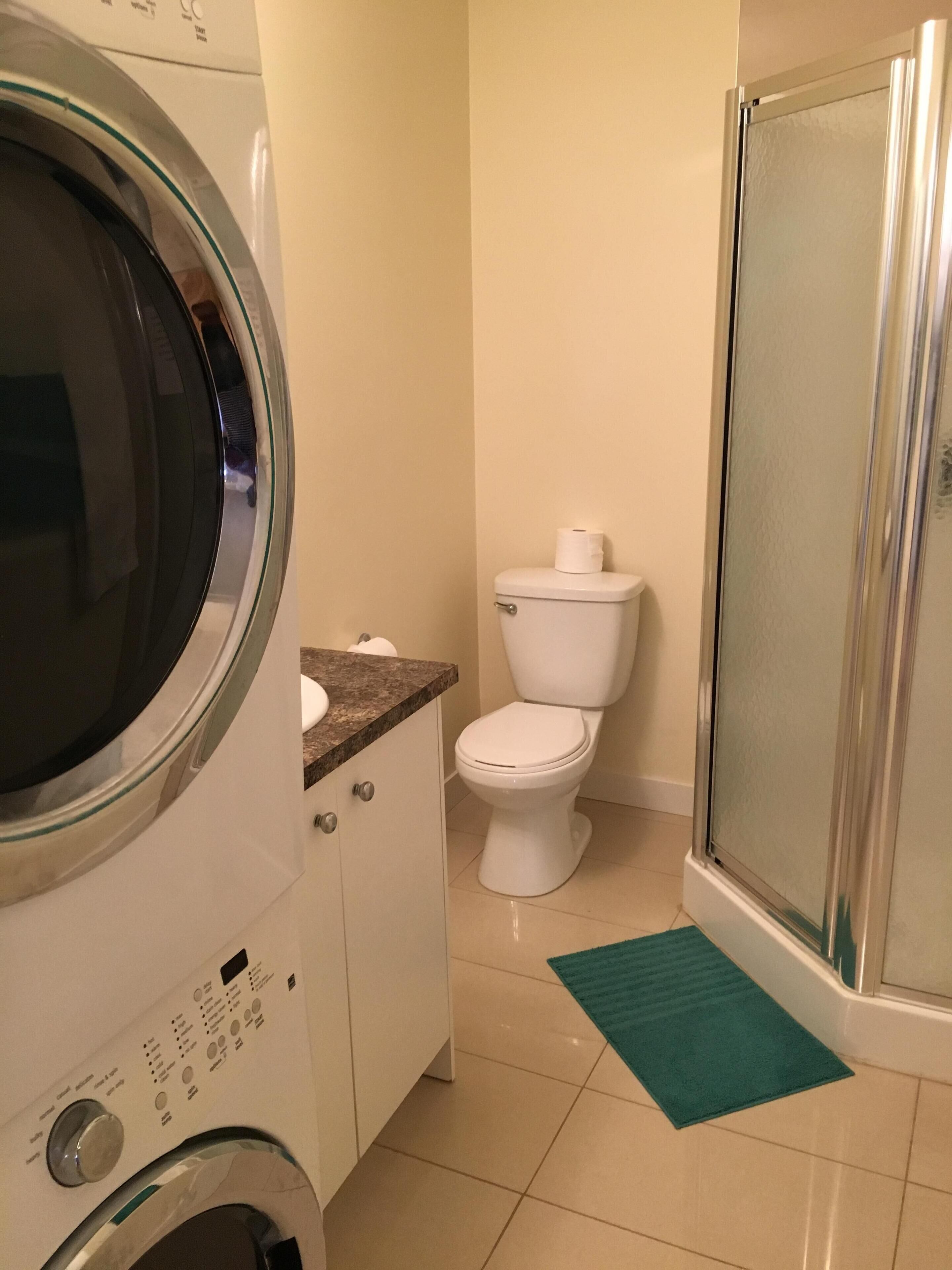 Une petite salle de bain équipée d’un lave-linge, de toilettes et d’une douche à parois en verre.