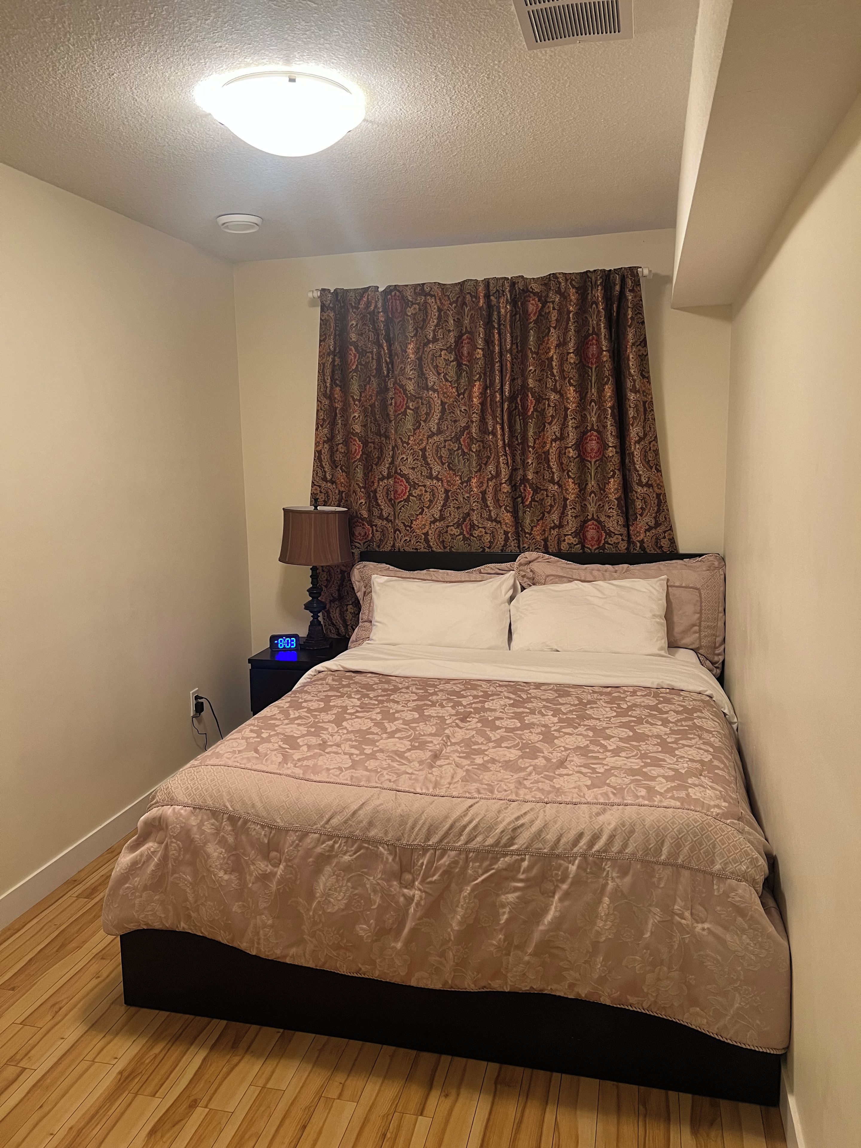 Une chambre à coucher avec un lit, une table de chevet, une lampe et une bouche d’aération fixée au mur.