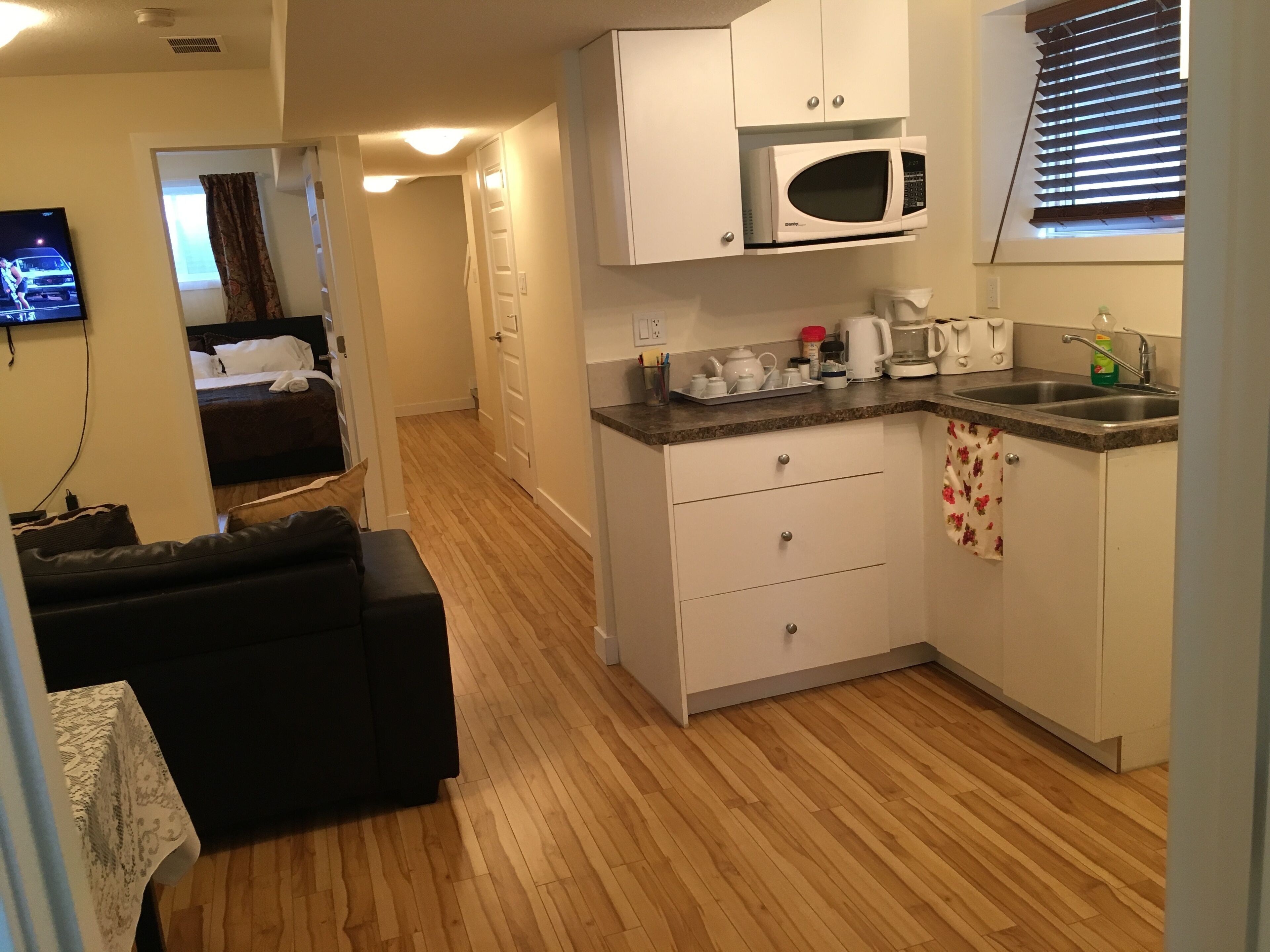 Una habitación de hotel compacta con kitchenette, televisor de pantalla plana, sofá y piso de madera.