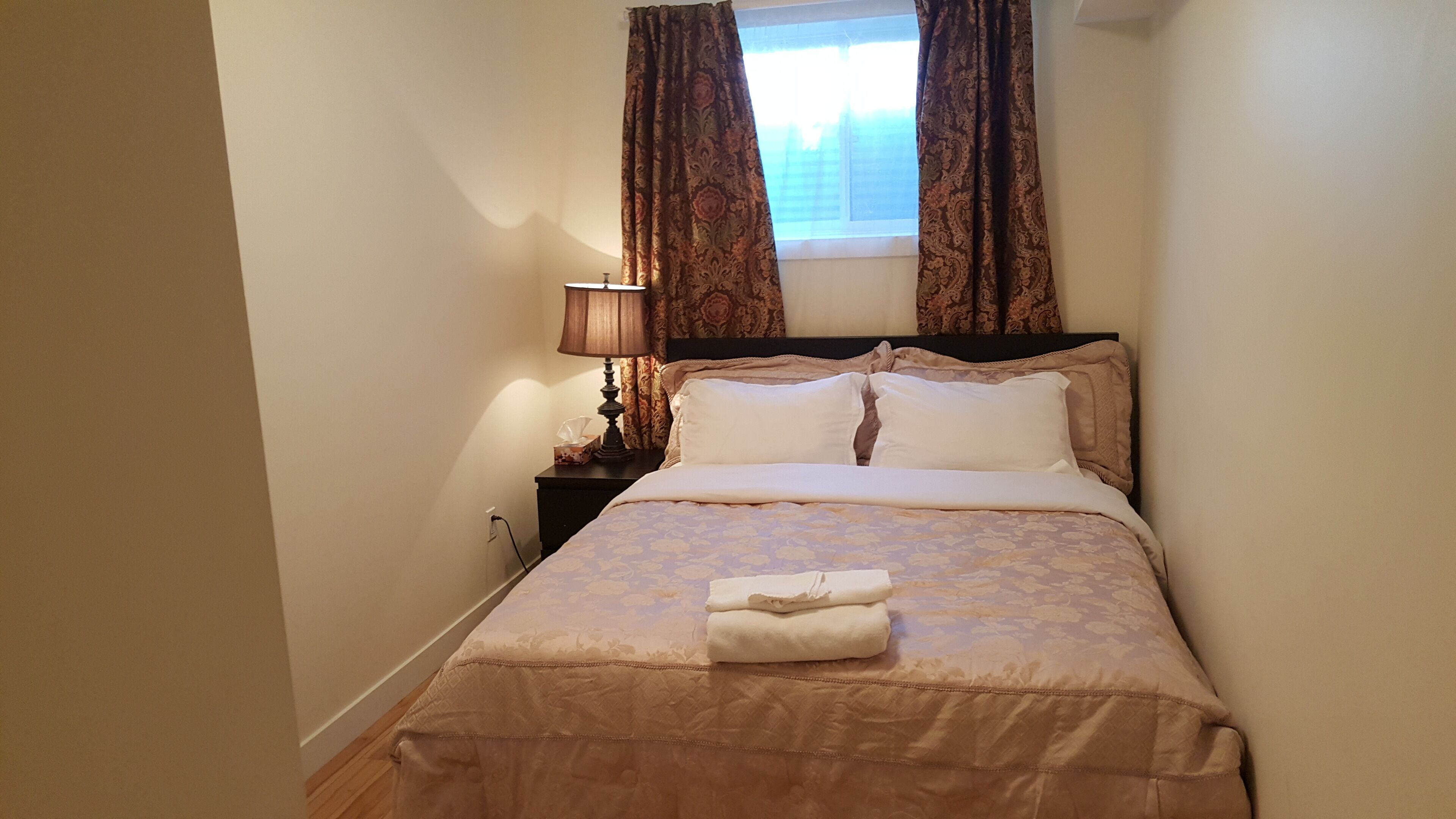 A neatly made bed with a floral bedspread, a bedside lamp, and a window with curtains.