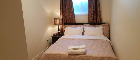 A neatly made bed with a floral bedspread, a bedside lamp, and a window with curtains.