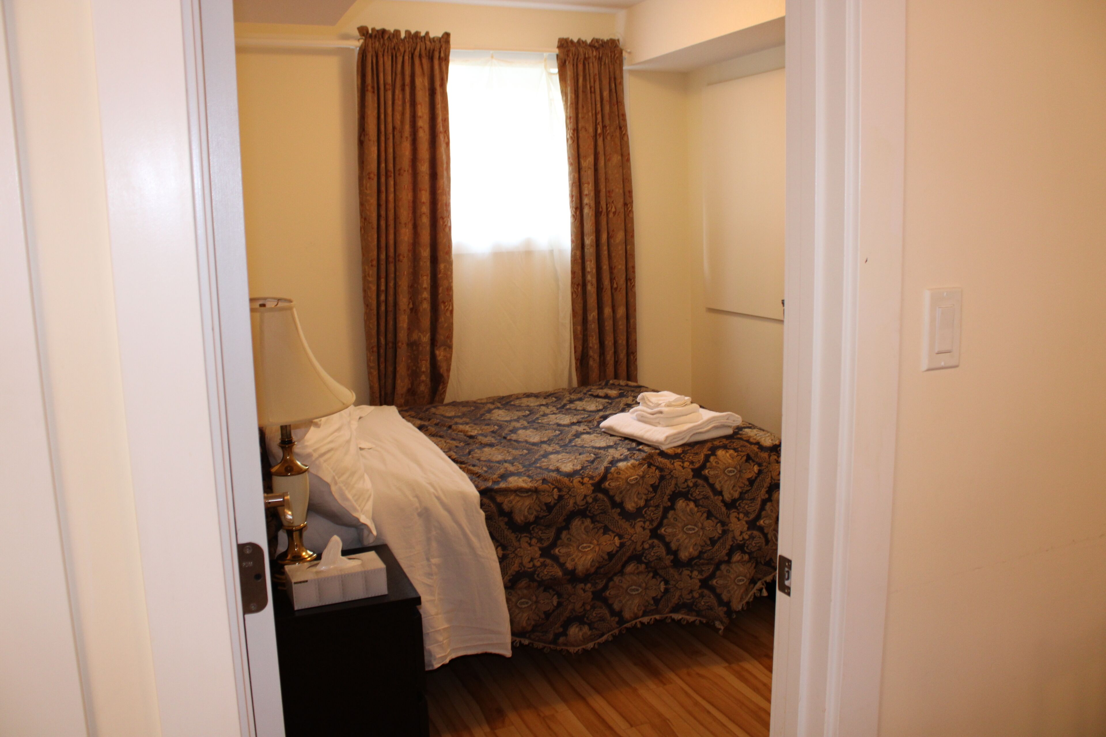 A bedroom with a bed, a nightstand, a lamp, and a window with curtains.