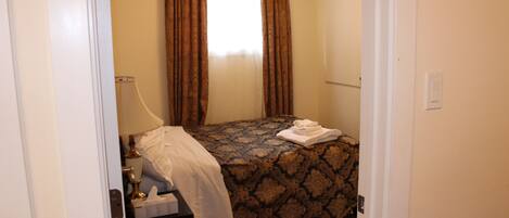 A bedroom with a bed, a nightstand, a lamp, and a window with curtains.