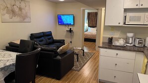 Ein kompakter Wohnbereich mit Sofa, Esstisch, Küchenzeile und einem an der Wand montierten Fernseher.
