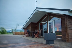 Une cabane moderne en bois, dotée d’une terrasse, de meubles d’extérieur et d’une grande porte-fenêtre coulissante.