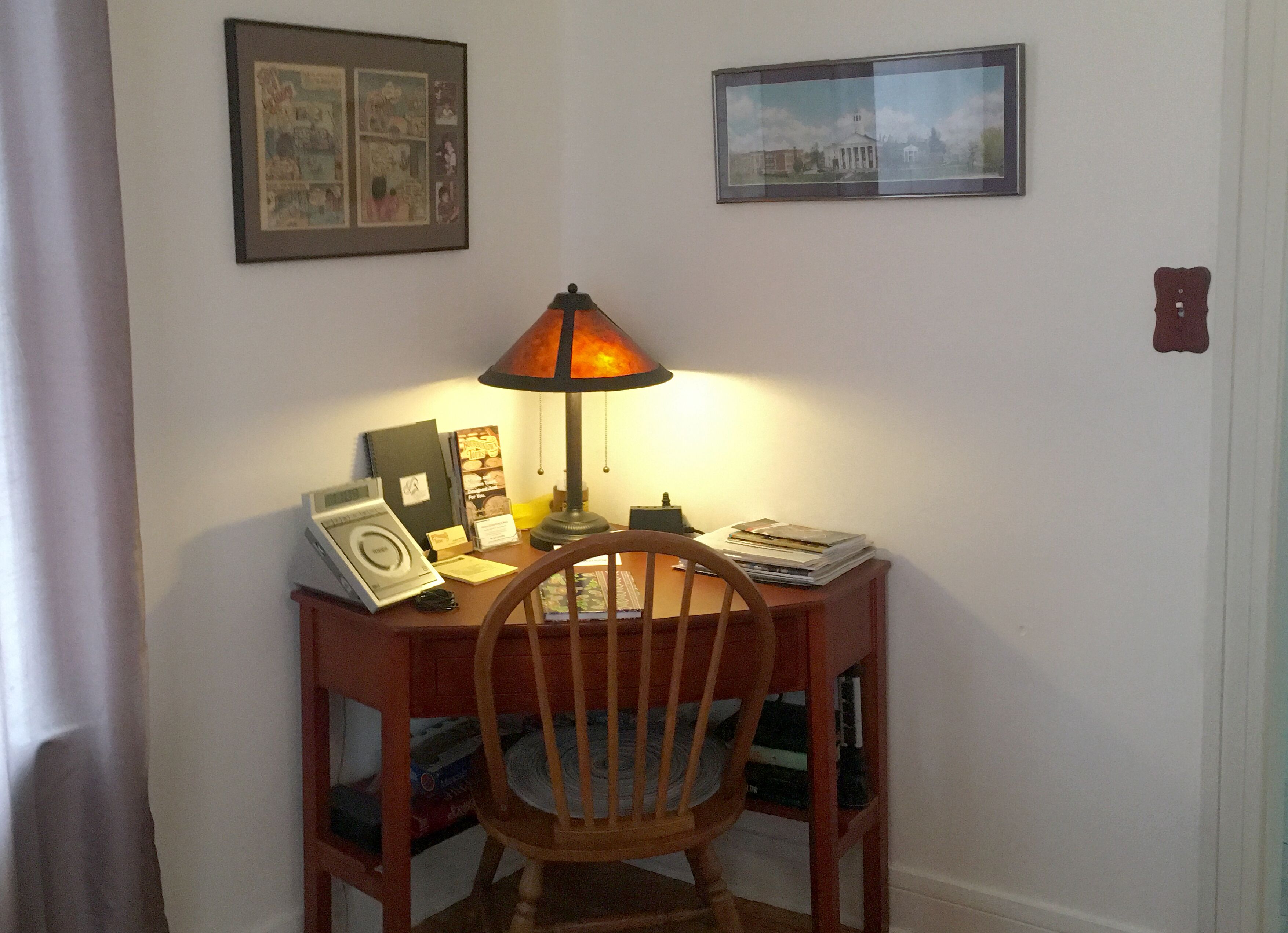 Ein Holztisch mit Lampe, einem Stuhl und verschiedenen Gegenständen, darunter ein gerahmtes Bild, ein Buch und eine Schachtel.