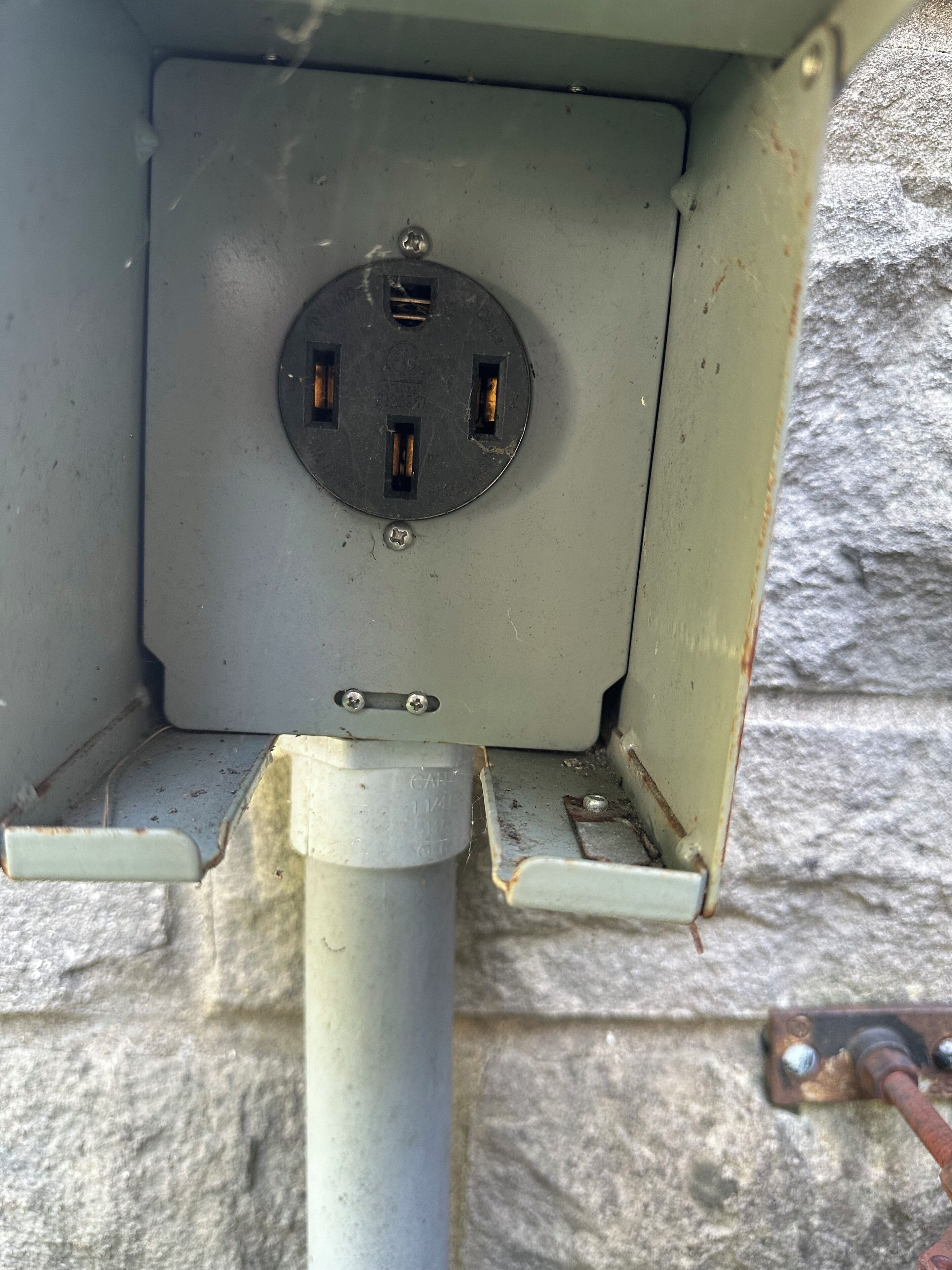 Een elektriciteitskast met een ronde stekkerdoos, een metalen pijp en een stenen muur.