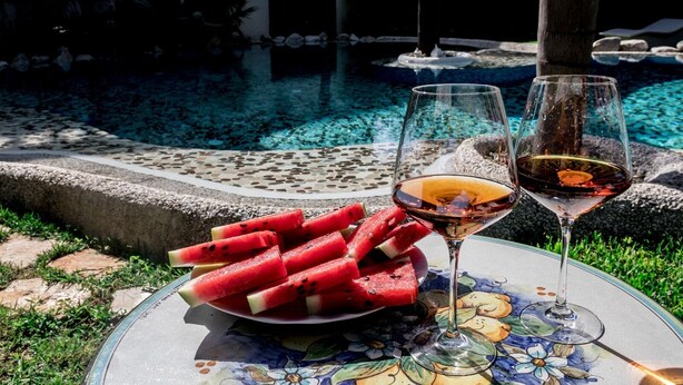 A table with watermelon slices and two wine glasses on a floral tablecloth near a pool. - Villa immersed in the Green (Pellaro)
