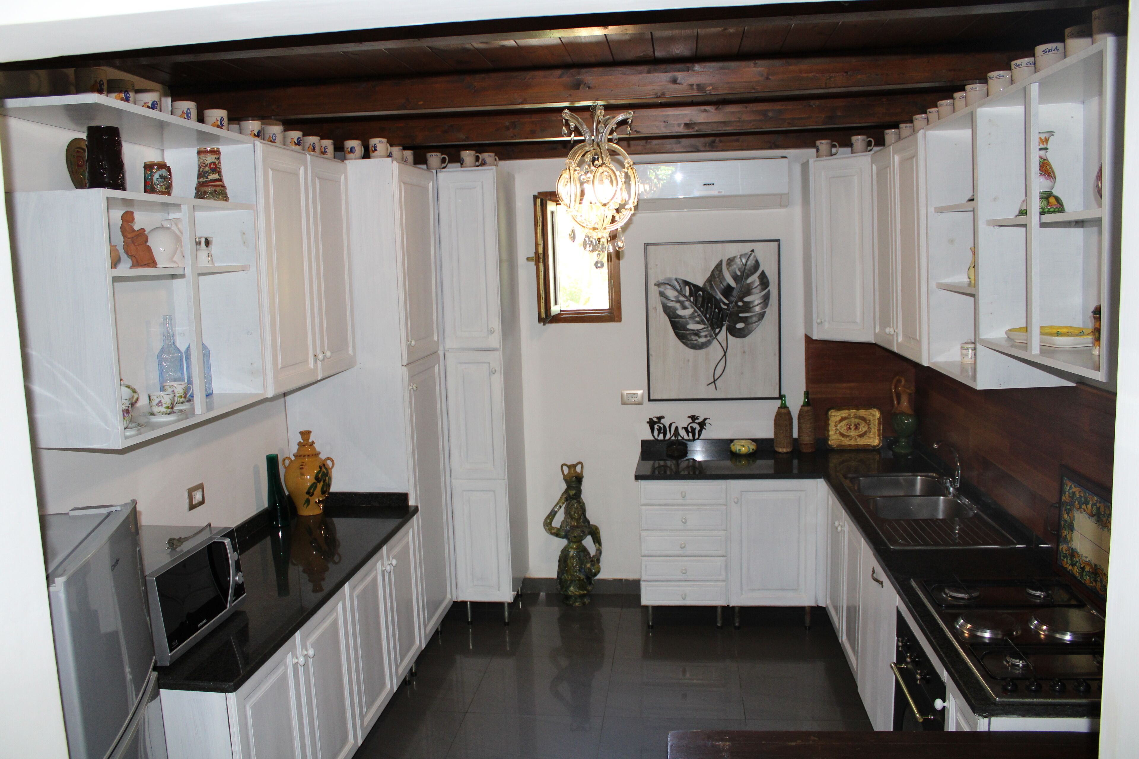 A compact kitchen with white cabinetry, a black countertop, and a central chandelier.