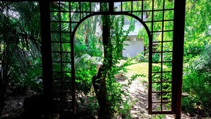 A garden with a stone pathway leading to a building through a metal gate. - Villa immersed in the Green (Pellaro)